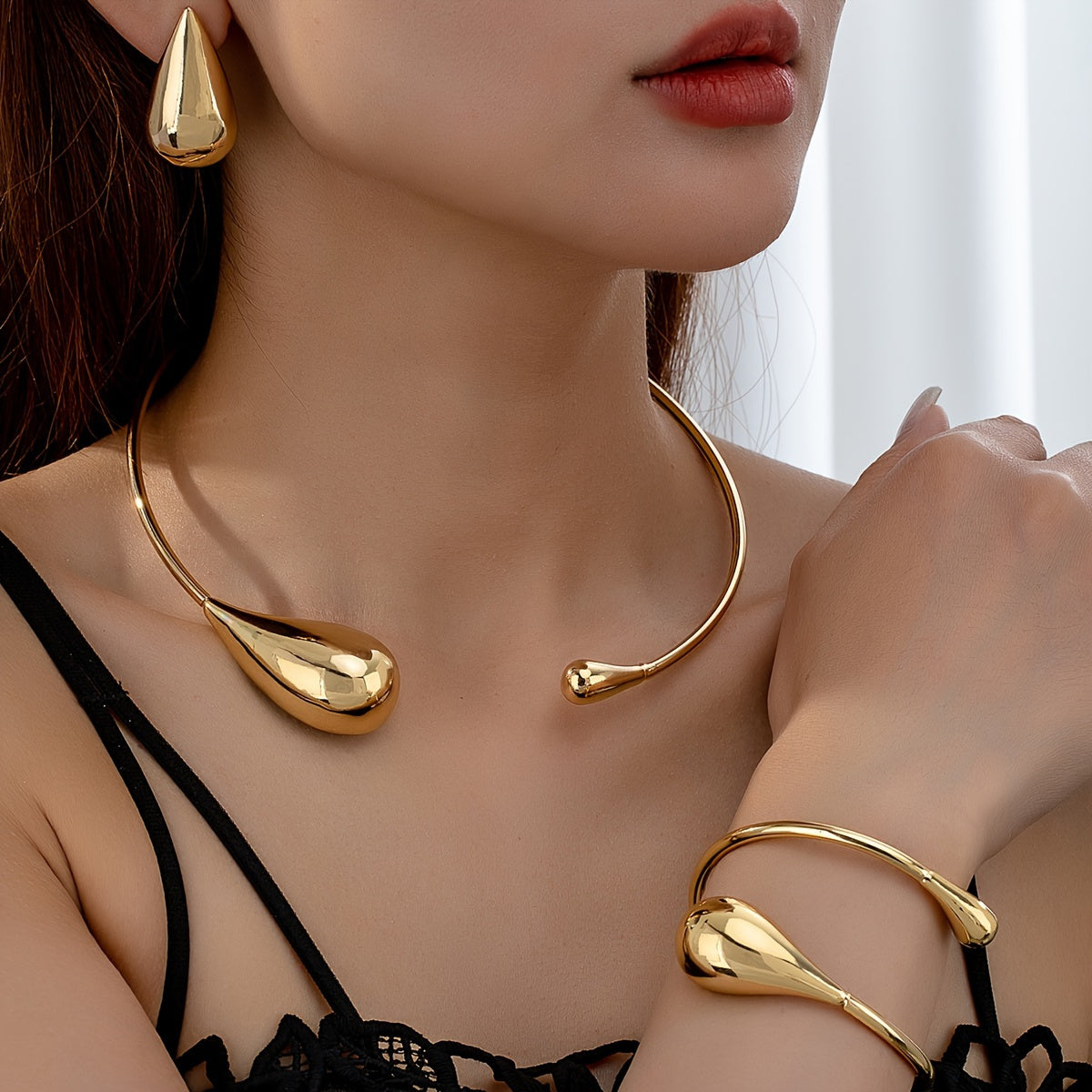 Close-up of HighPeak Teardrop Jewelry Set in polished gold worn with a black top, featuring sculpted necklace, bracelet, and earrings.