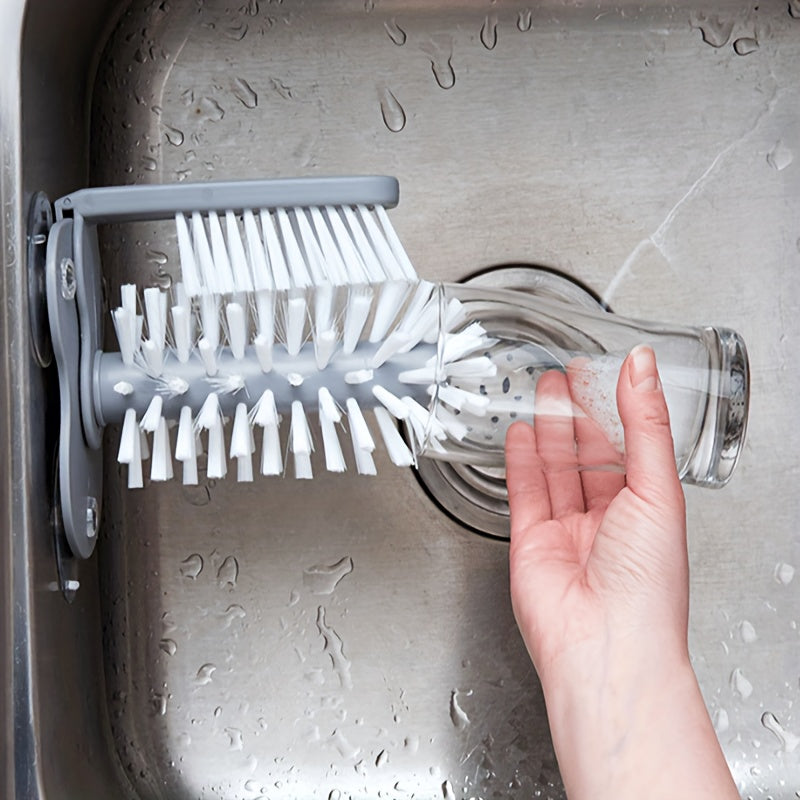 TwistClean™ Cup & Glass Scrubber in gray mounted on sink, cleaning a clear glass with flexible bristles and suction base