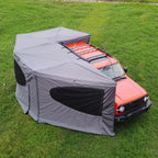 270° Vehicle Awning Tent extending around the side and rear of an orange vehicle on grass.