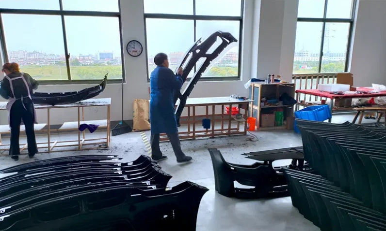 Supplier workshop showing workers handling automotive body components at worktables.