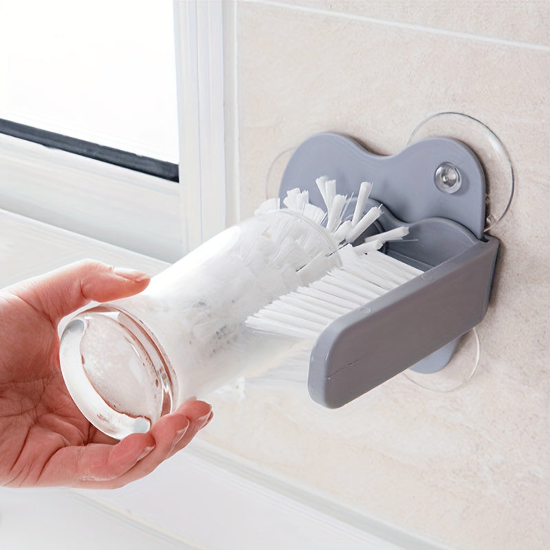 TwistClean™ - Cup & Glass Scrubber mounted on sink wall with white bristles cleaning a clear glass cup by hand