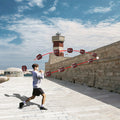GripEgg™ Trainer – PASS & CATCH Edition in brown with white laces, thrown by a young man outdoors near a lighthouse wall.
