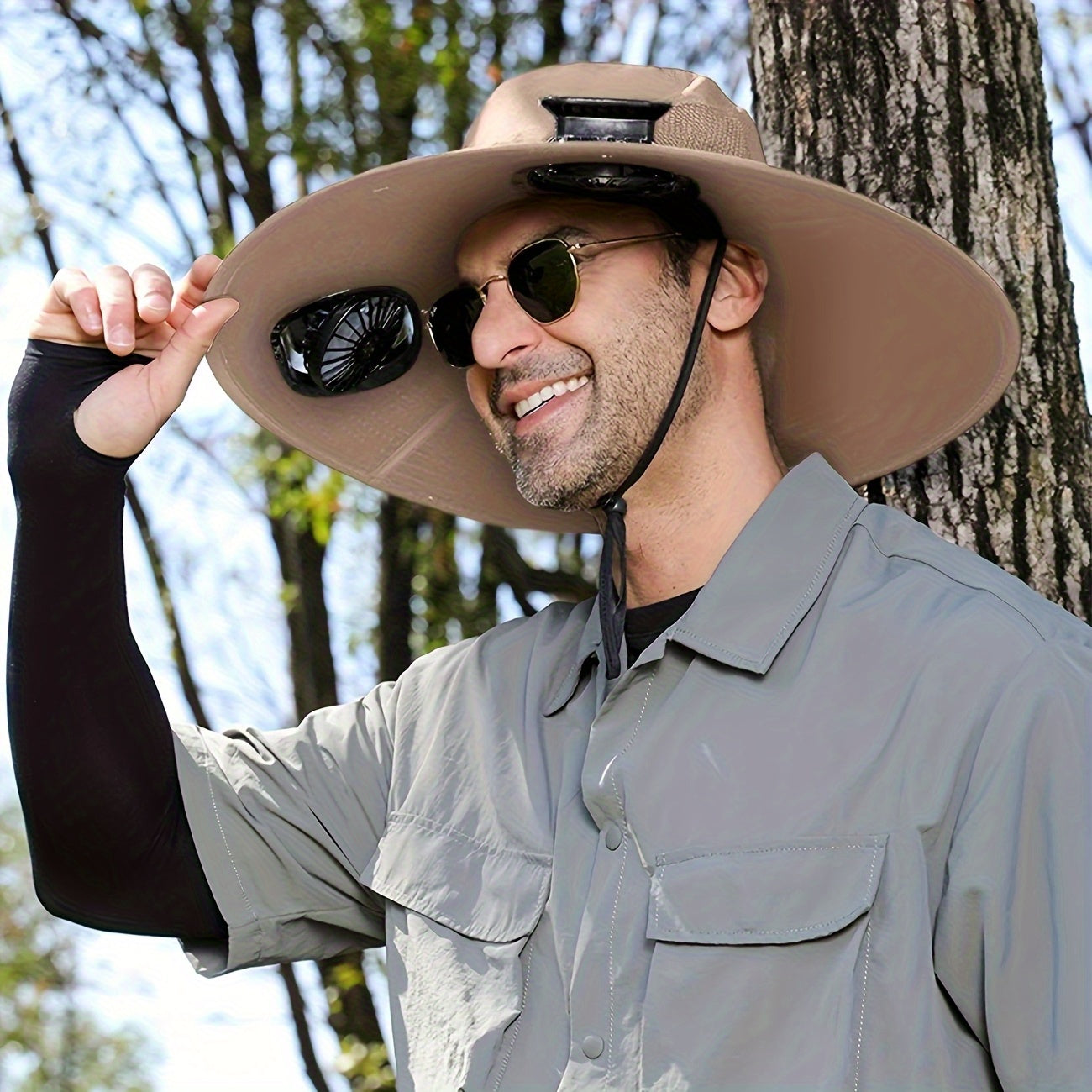 HighPeak Cooling Fan Sun Hat in tan with dual fans worn outdoors by man beside tree on sunny day