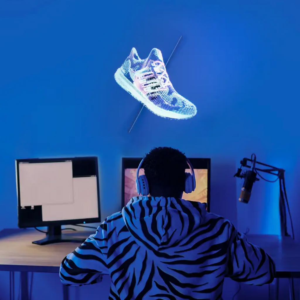 HighPeak AirAura displaying holographic sneaker with blue glow effect above dual-monitor gaming setup in dark room
