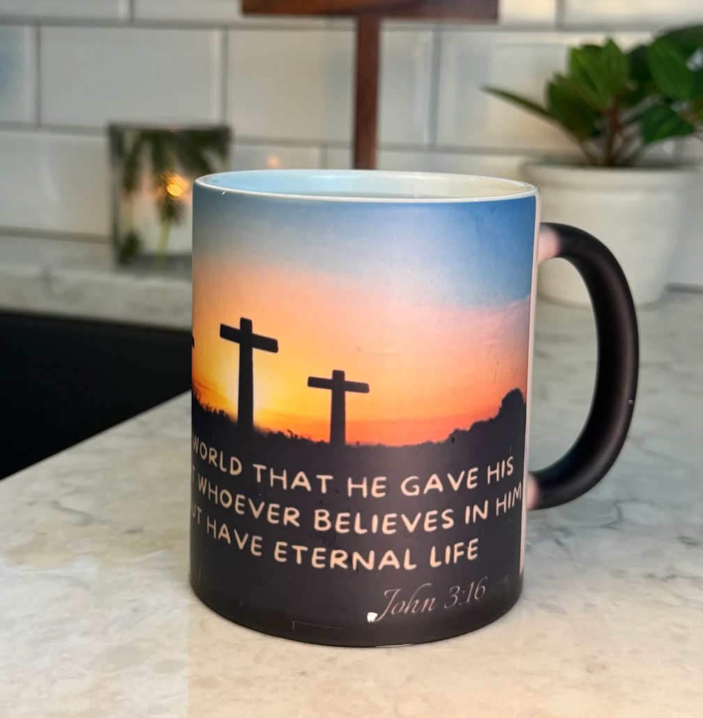 FaithGlow Mug featuring John 3:16 verse against sunset sky with crosses silhouette on marble counter, heat-reactive ceramic design