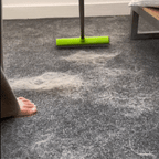 FurSweep Pro broom with bright green rubber head collecting pet hair from dark gray carpet, demonstrating cleaning action