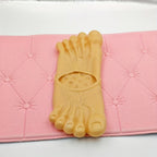 Giant Feet Slippers in realistic beige design with detailed toes and veins displayed on pink cushioned surface