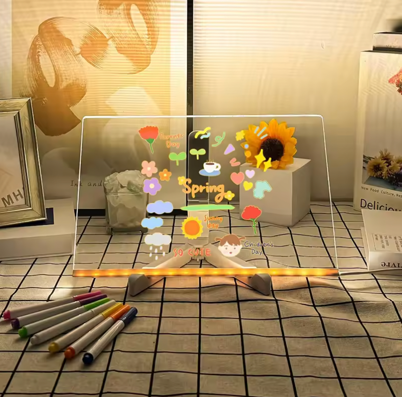 GlowSketch Board displaying illuminated spring flowers and sunflowers on transparent surface with colored markers on tiled surface
