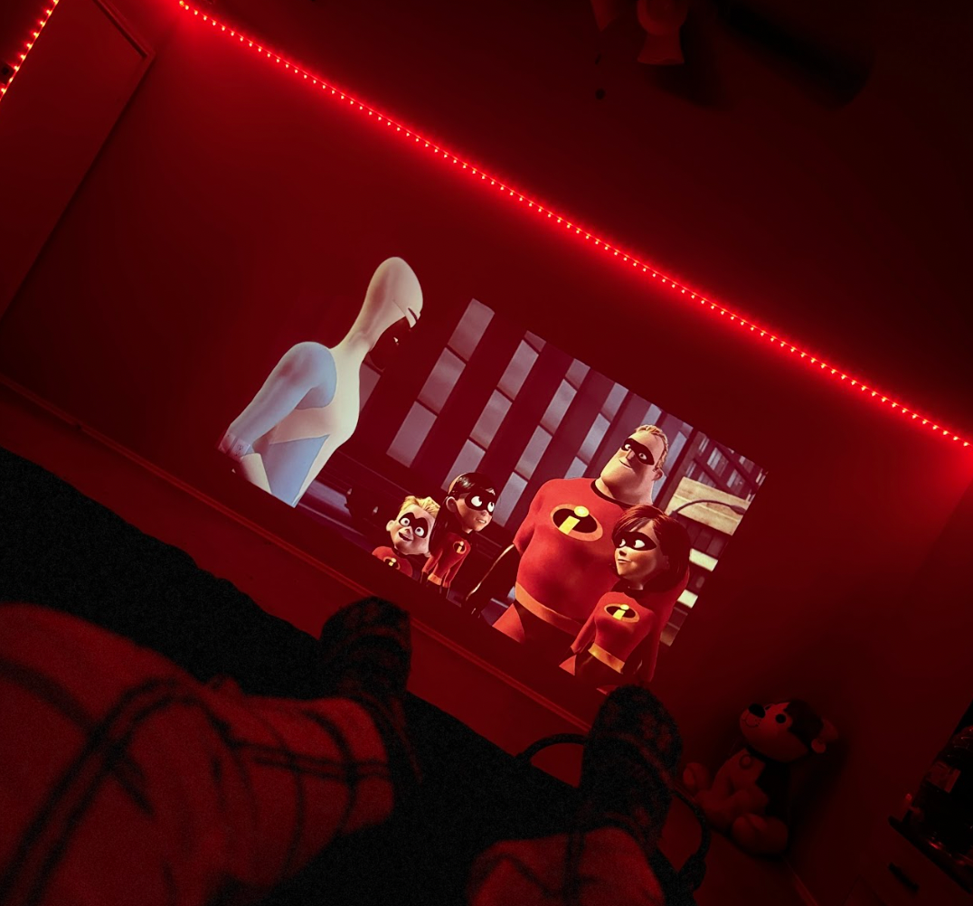 HighPeak INFINITY MiniProjector displaying animated movie scene in dark room with red LED ambient lighting on ceiling
