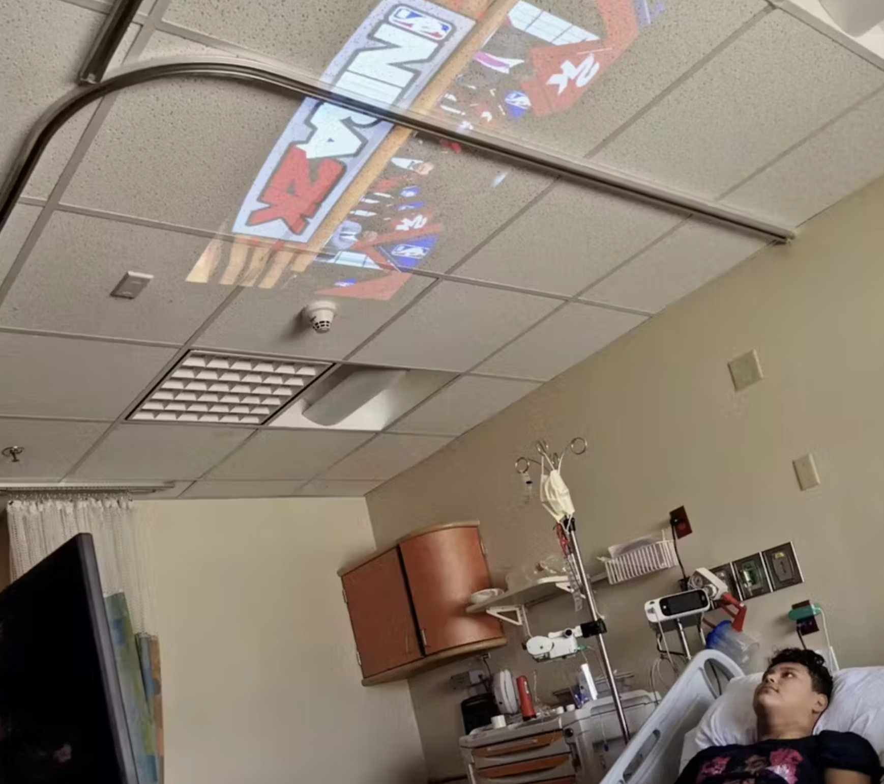 HighPeak INFINITY Projector Plus projecting a colorful video onto a hospital ceiling from a bedside setup
