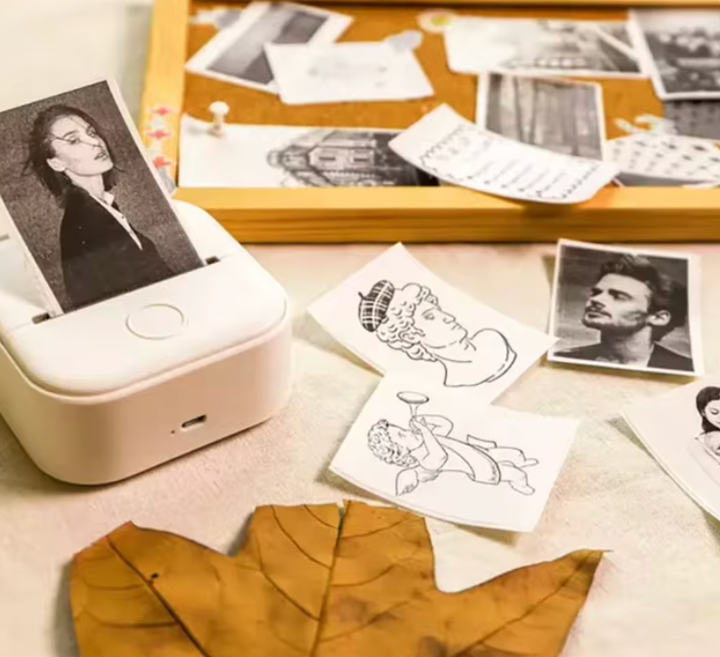 HighPeak MiniPrinter in white shown with printed photos and sketches scattered on desk with autumn leaves