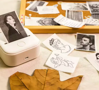 HighPeak MiniPrinter in white shown with printed photos and sketches scattered on desk with autumn leaves
