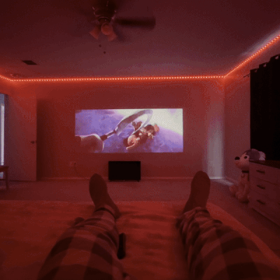 HighPeak MiniProjector™ projecting a movie on a wall in a cozy dimly lit room with red LED accent lighting