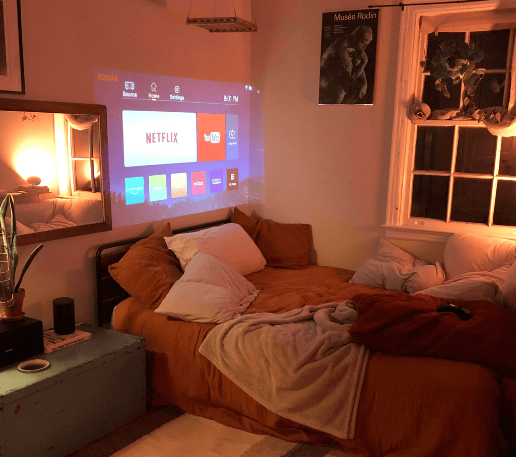 HighPeak MiniProjector projecting Netflix interface on a bedroom wall with cozy warm lighting and soft bedding surroundings