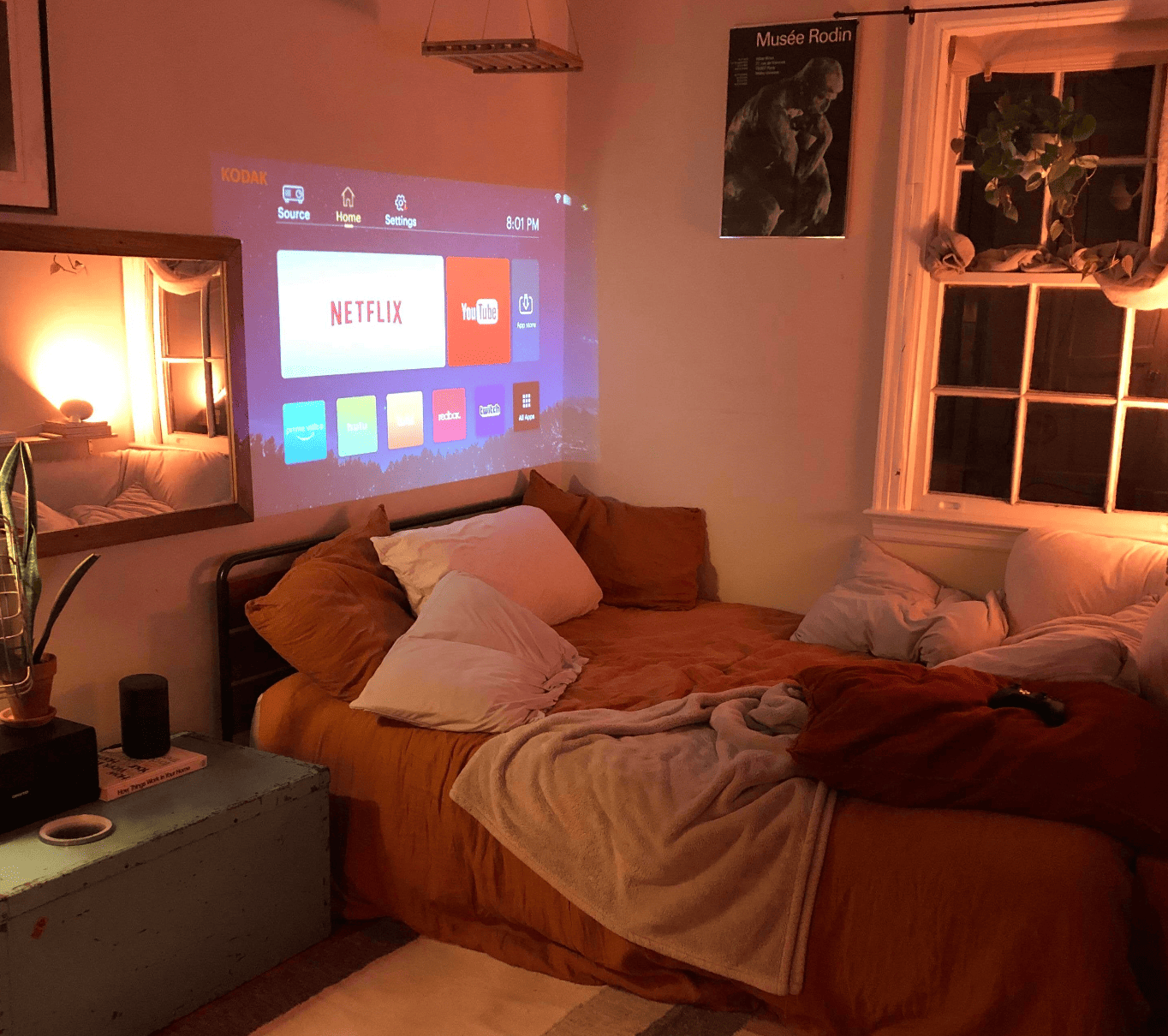 HighPeak MiniProjector displaying Netflix menu on wall, cozy bedroom setup with warm lighting and brown bedding