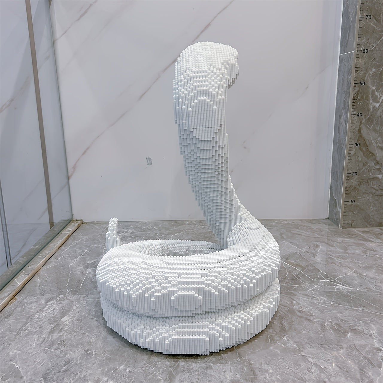 HighPeak SerpentMaster white coiled snake sculpture built from 5000 building blocks on marble floor against marble wall