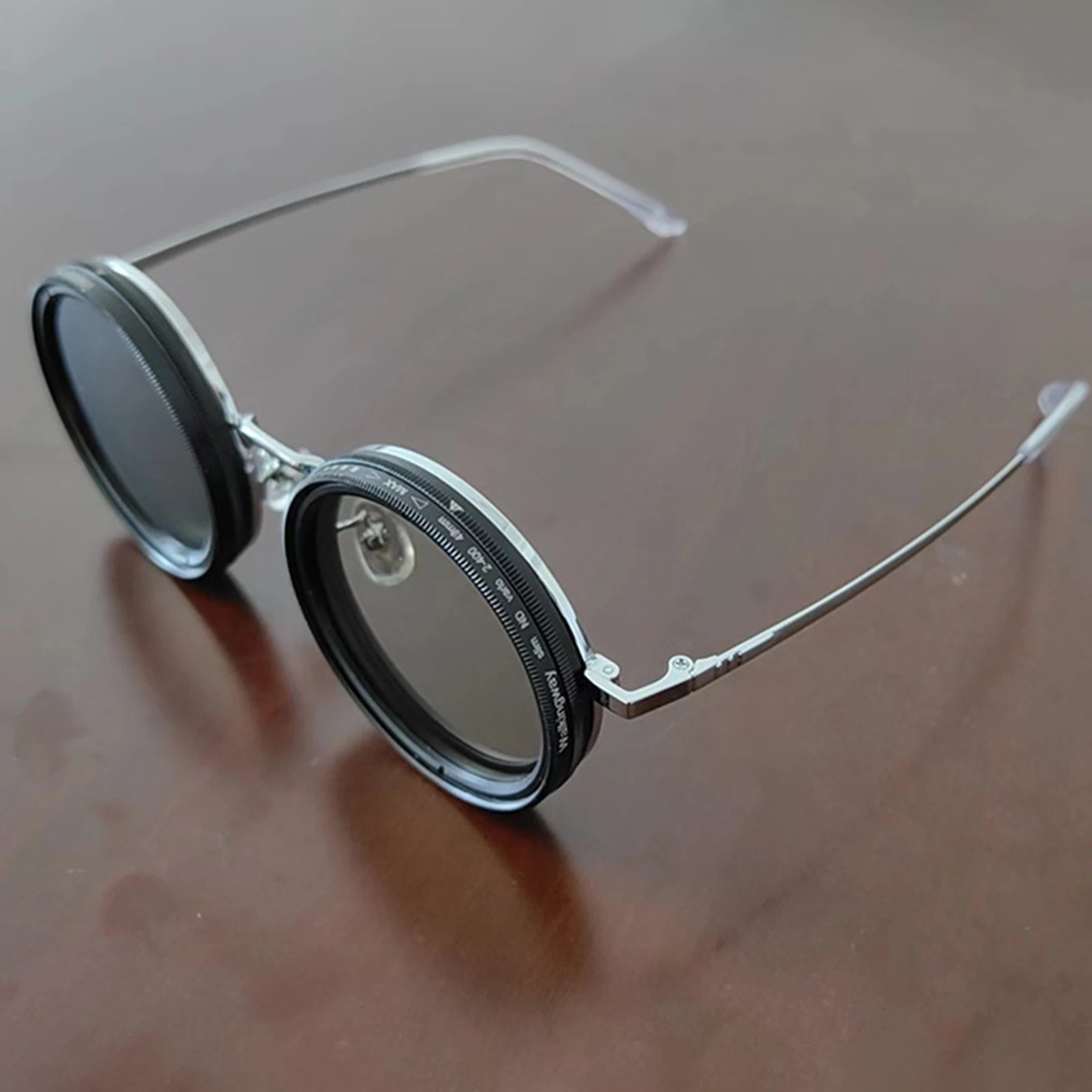 HighPeak ShiftLens round sunglasses with adjustable 9-in-1 lens system in black frame and silver temple arms on wooden surface