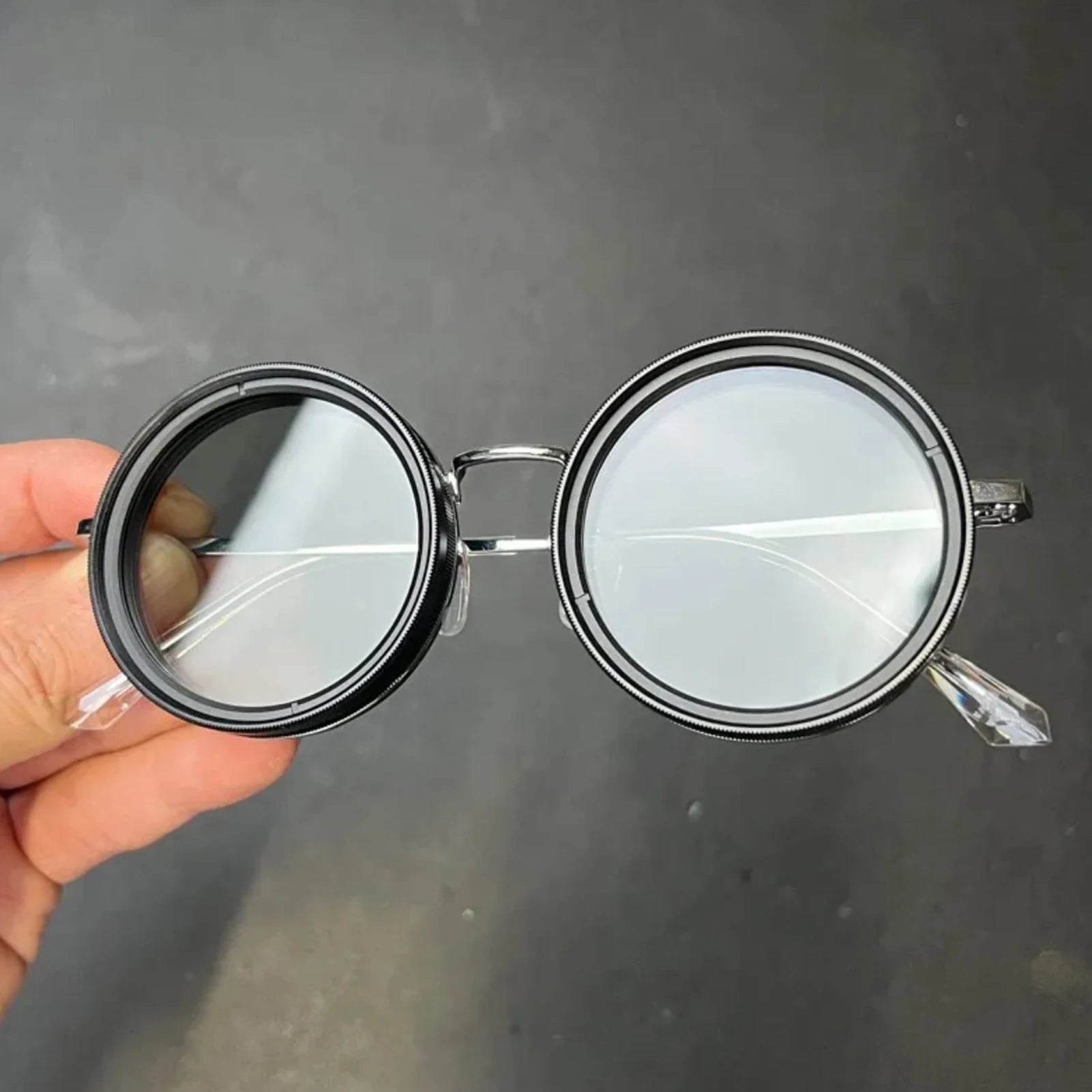 HighPeak ShiftLens™ round sunglasses with black metal frame and adjustable clear lenses shown in hand against dark background