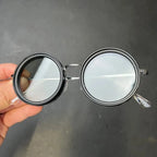 HighPeak ShiftLens™ round sunglasses with black metal frame and adjustable clear lenses shown in hand against dark background
