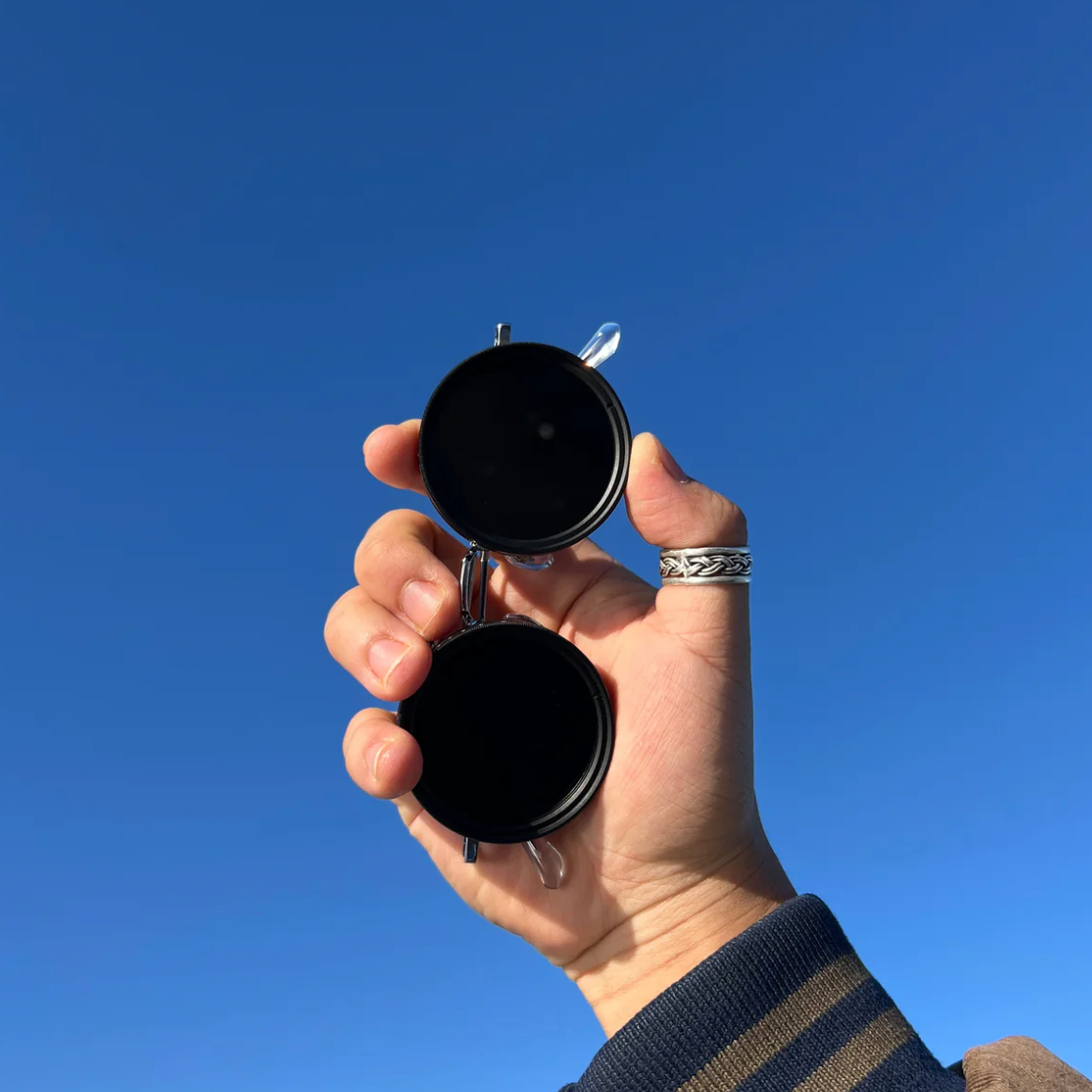 HighPeak ShiftLens sunglasses with black adjustable lenses held up against vibrant blue sky - adaptive eyewear demonstration