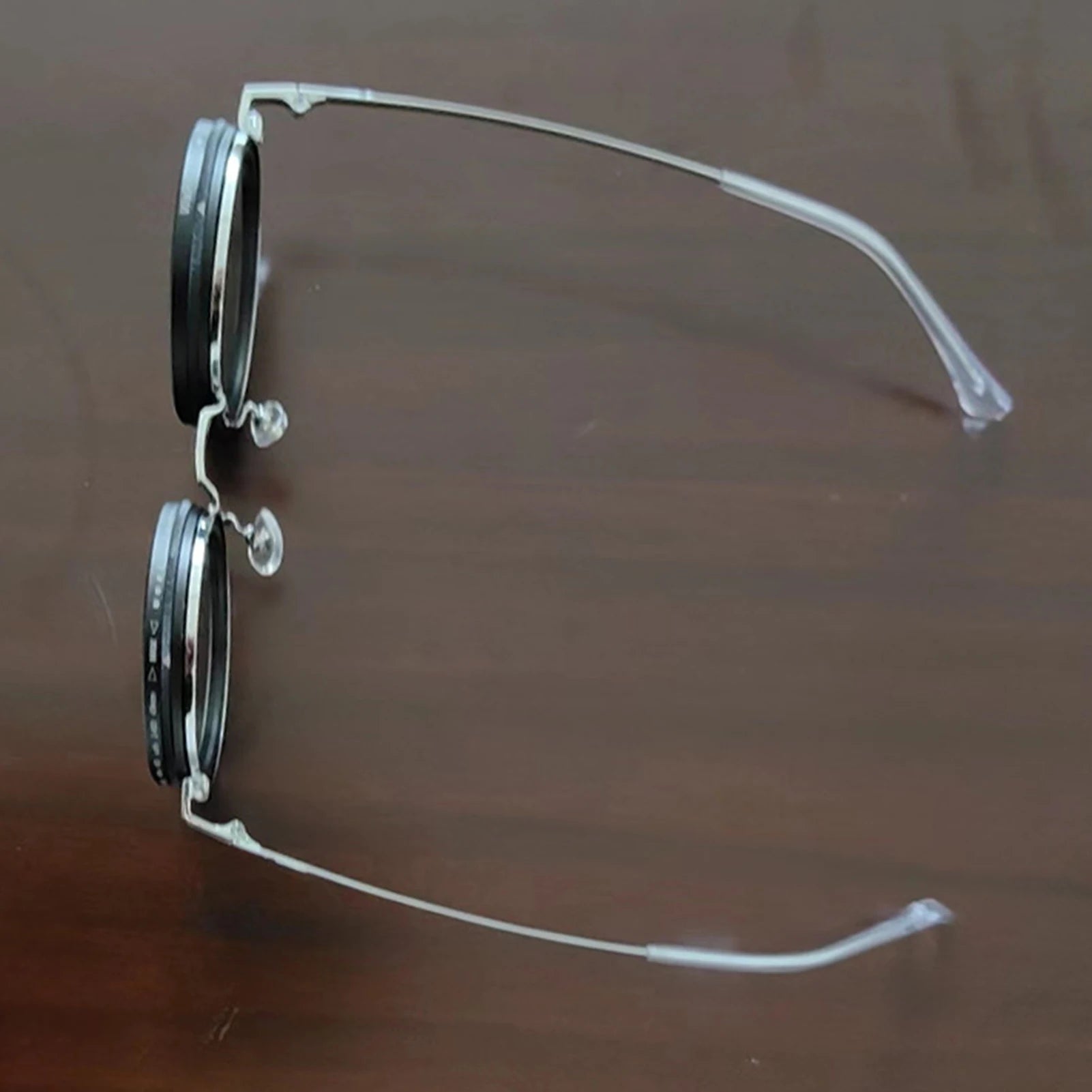 HighPeak ShiftLens sunglasses with silver frame and adjustable 9-in-1 lens system shown in side profile on wooden surface