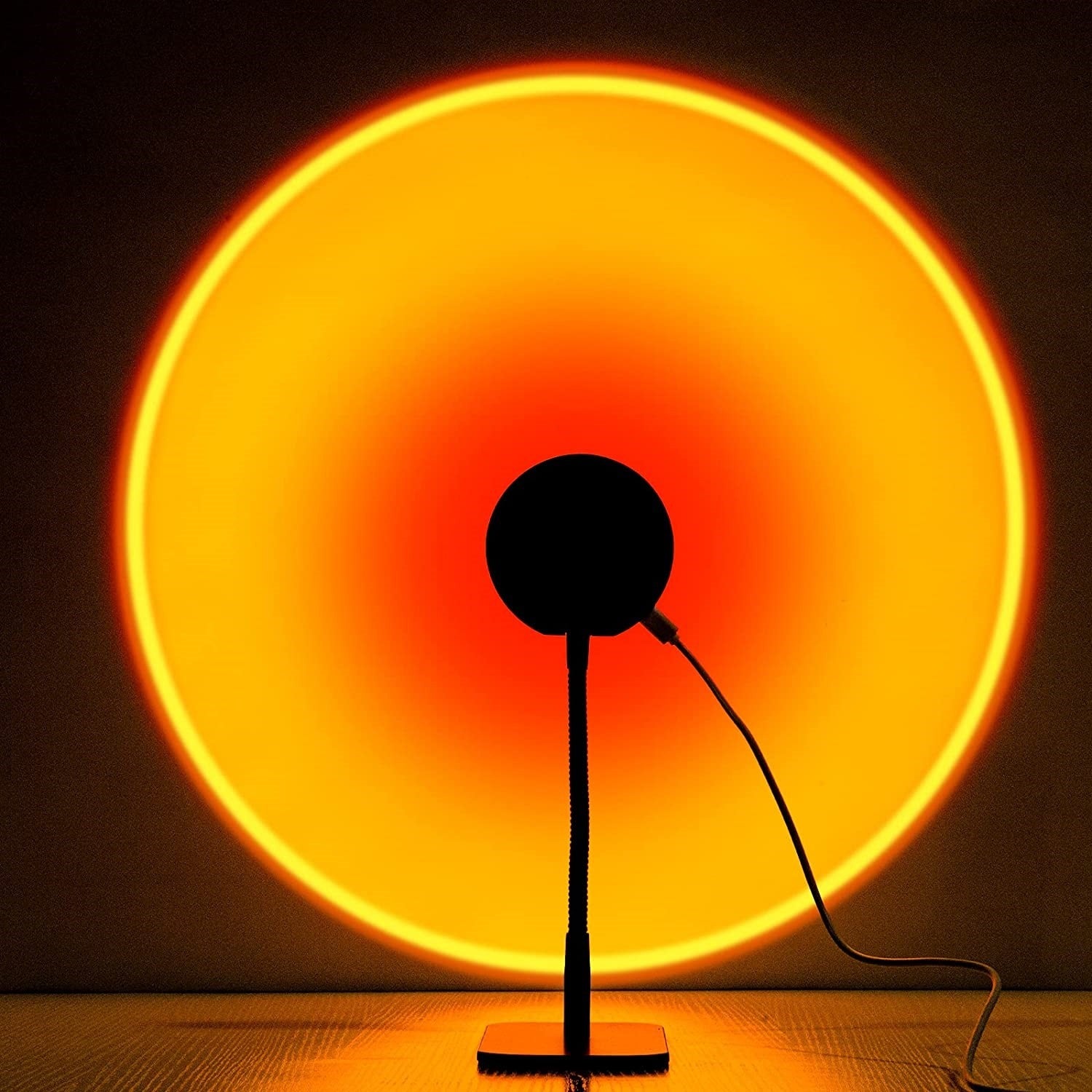 HighPeak Sunset Lamp projecting vibrant orange-red circular glow with black stand on wooden surface - modern ambient lighting
