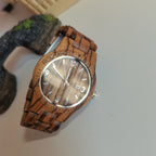 HighPeak TimberTime handcrafted zebra wood watch with brown face and silver hands displayed on dark textured surface