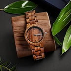 HighPeak TimberTime zebra wood watch with calendar display on wooden stand, surrounded by green leaves on black surface