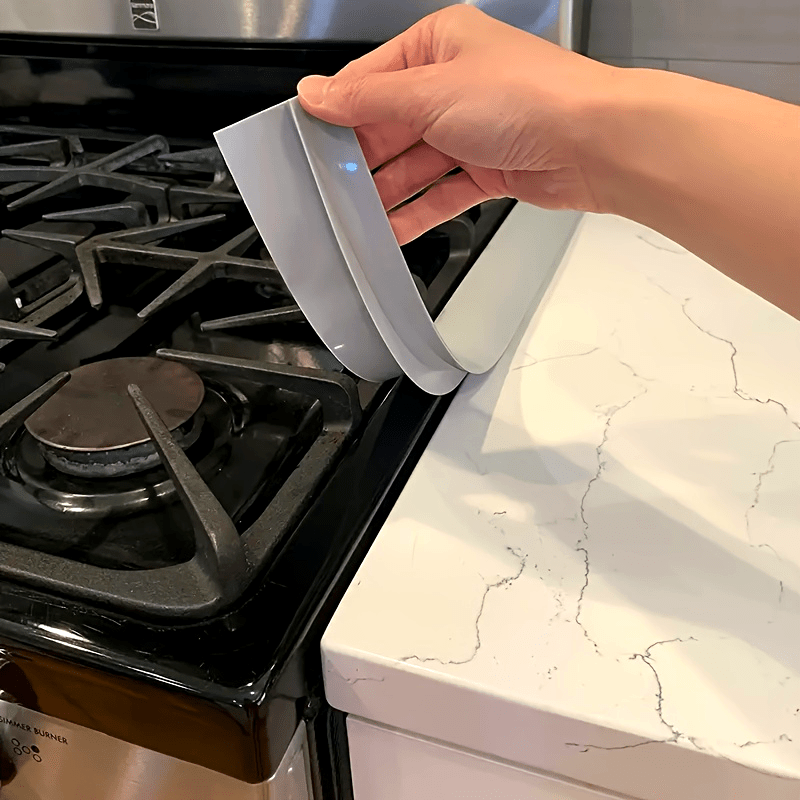 Kitchen Gap Guard silicone cover being placed between stove and counter to prevent crumbs and spills from falling through gap
