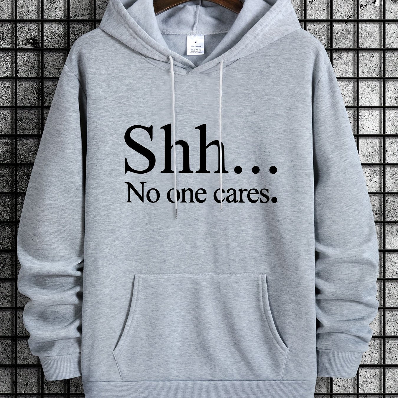 Light gray pullover hoodie with Shh No One Cares text print and kangaroo pocket on clothing display