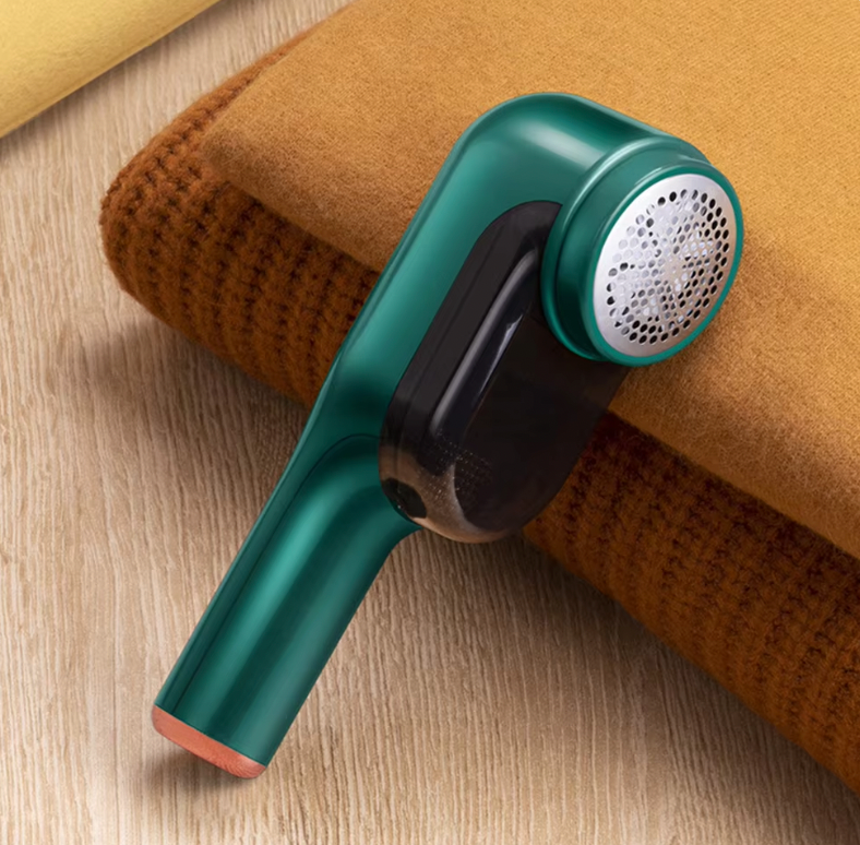 LintBuster Pro in sleek teal design removing lint from orange knit sweater on wooden surface - portable fabric shaver