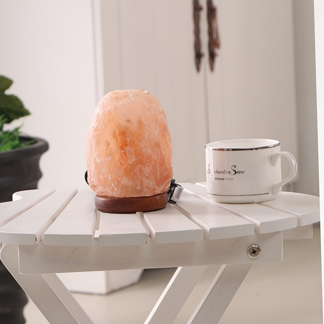 LumiStone Himalayan salt lamp glowing peacefully on white wooden table with ceramic coffee cup - natural wellness ambiance
