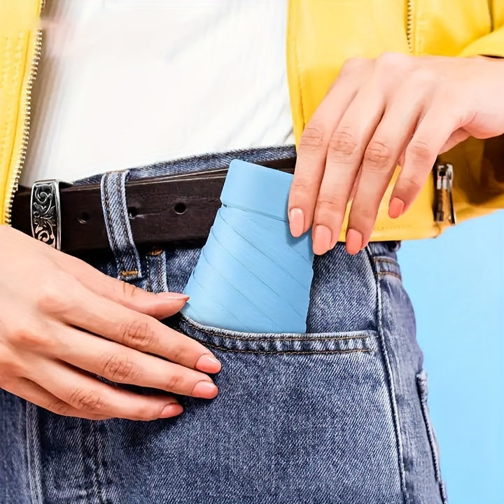 Mini Pocket Umbrella in light blue being placed into denim jeans pocket with yellow jacket detail showing compact size