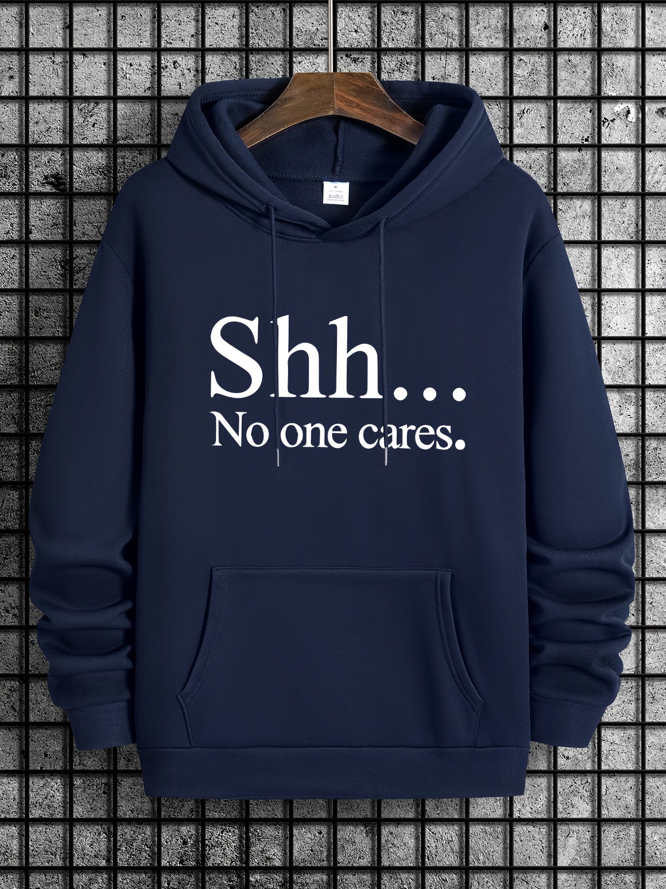 Navy blue Shh No One Cares hoodie with white text print, front kangaroo pocket on wooden hanger against tiled wall