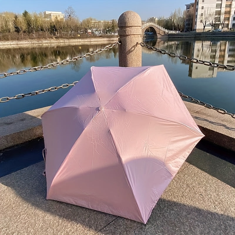Pink Mini Pocket Umbrella displayed at waterfront with stone bridge in background, reflecting urban landscape in water