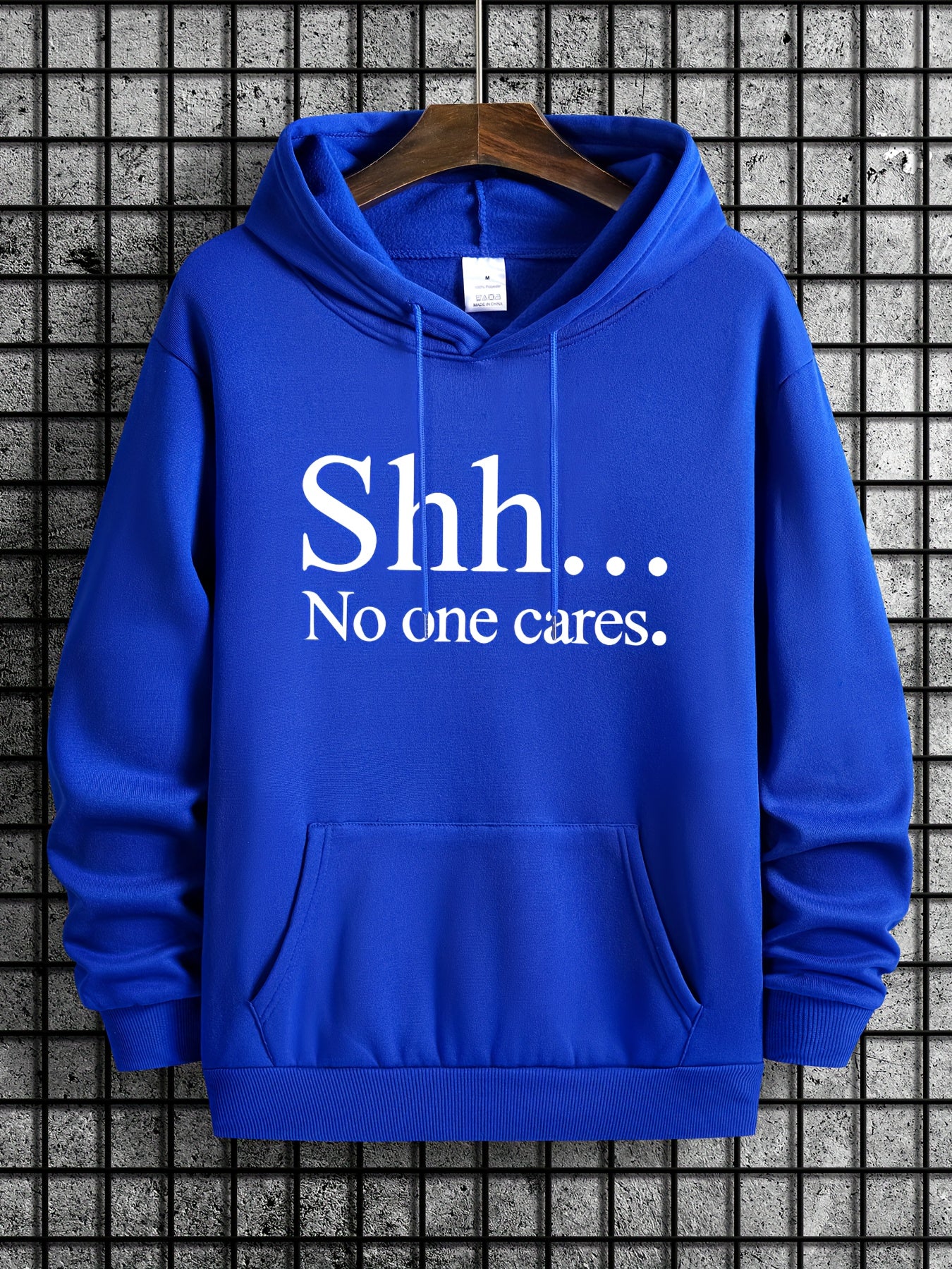 Royal blue Shh No One Cares hoodie with white text print and kangaroo pocket displayed on wooden hanger