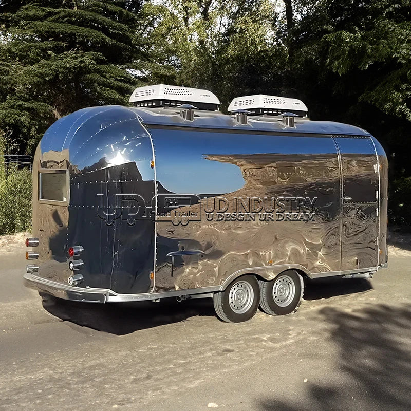 HighPeak Airstream Food Trailer with polished stainless steel exterior parked outdoors among trees, ready for food service.