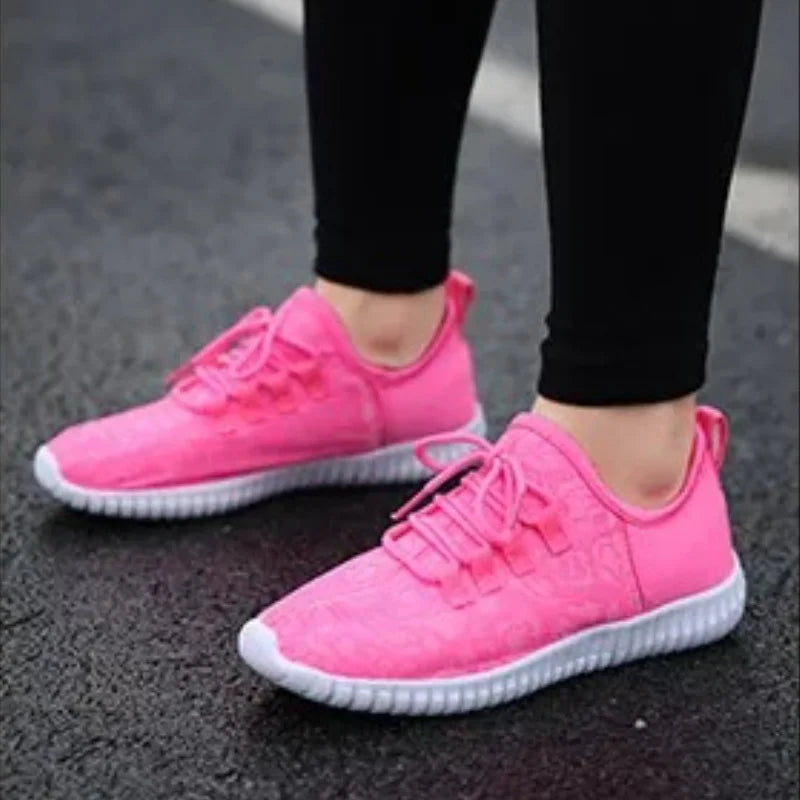 HighPeak Glowstride Sneakers in bright pink with white soles worn outdoors on asphalt with black leggings
