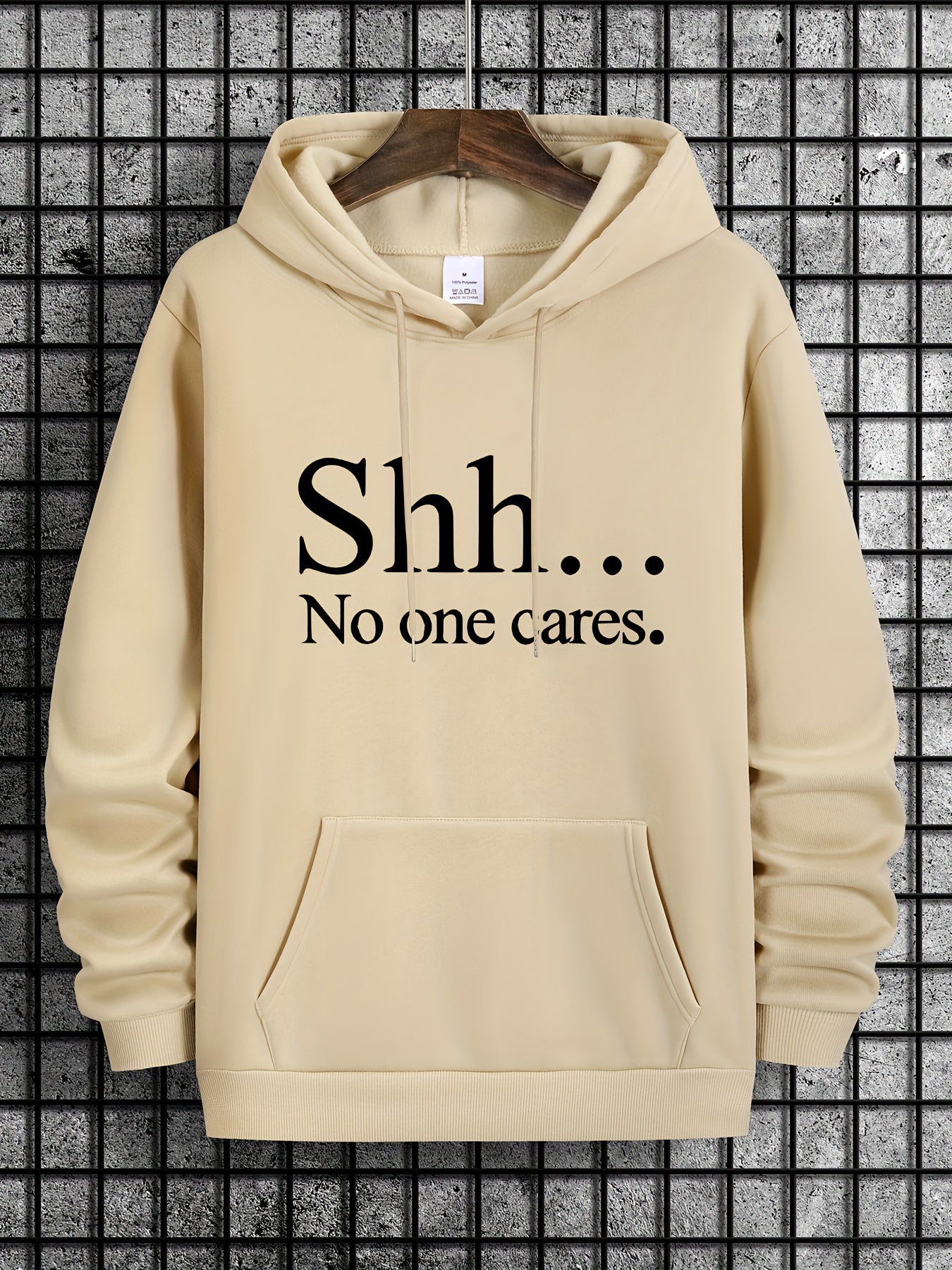 Shh No One Cares hoodie in beige with black text print, front kangaroo pocket and classic pullover style on display