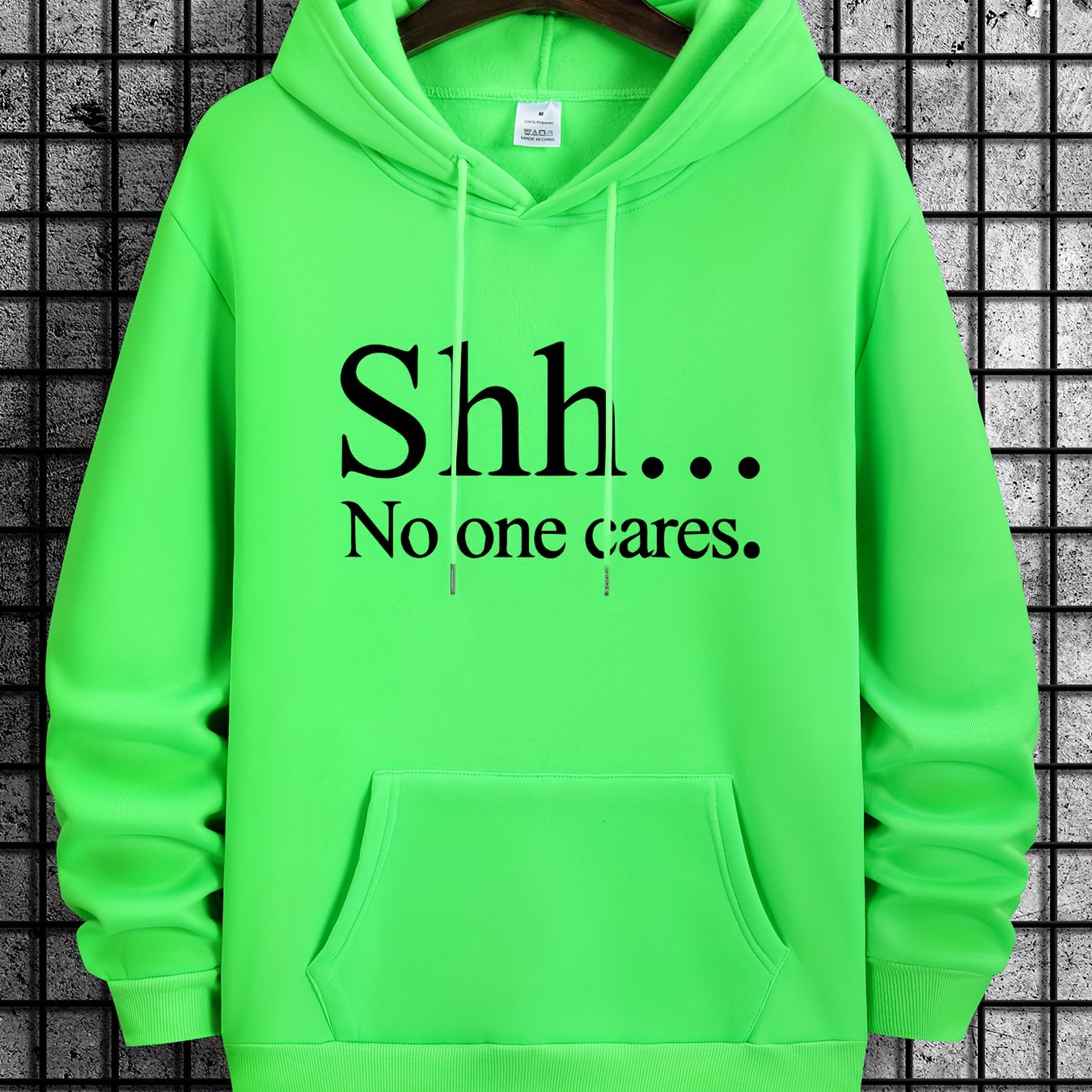 Shh No One Cares hoodie in neon green with black text print and kangaroo pocket on grey tile background