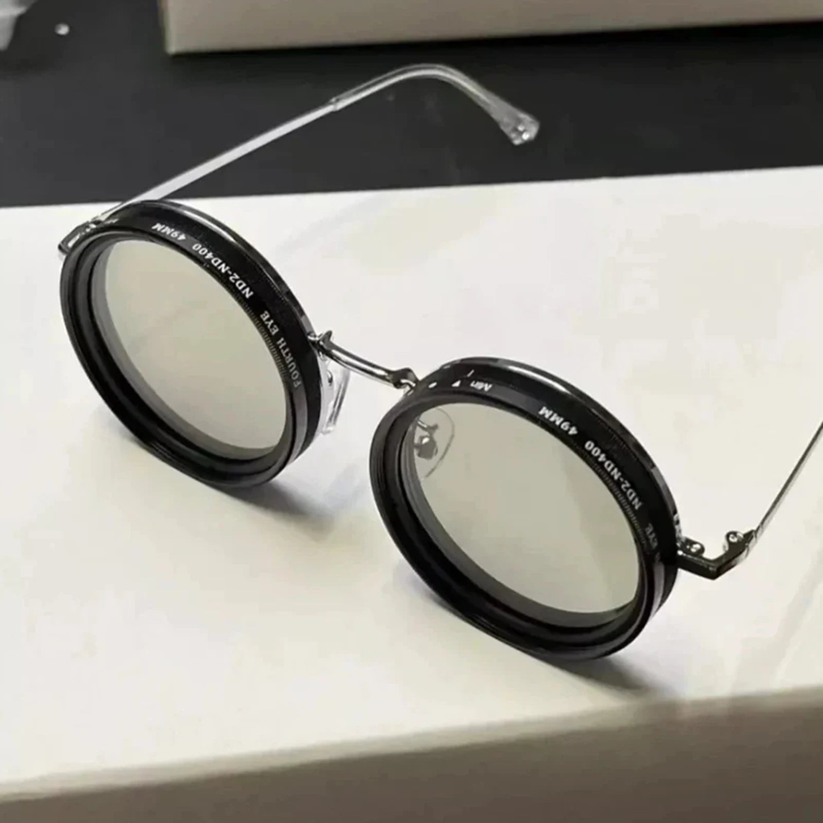 ShiftLens™ round sunglasses with black frames and adjustable light-filtering lenses on white surface - adaptive eyewear design