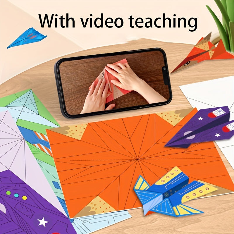 SkyGlide paper airplane kit with colorful pre-creased sheets, smartphone showing video tutorial, and completed planes on wooden desk