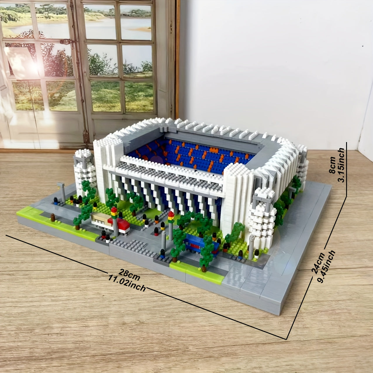 StadiumMaster miniature football stadium building set in white with blue interior and green landscaping on wooden surface