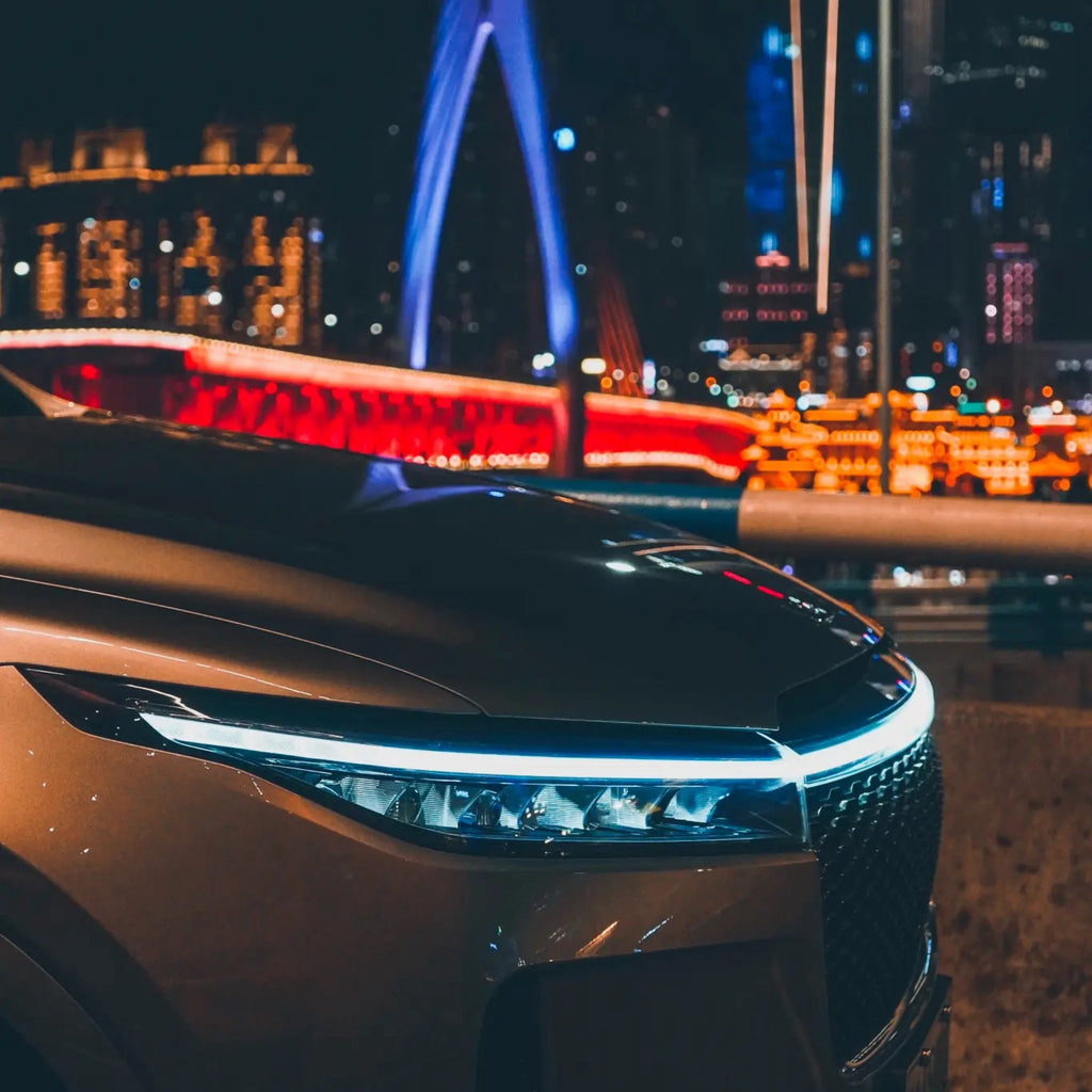 StrikeLine LED hood light strip illuminating sleek car front at night with cityscape and illuminated bridge background