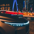 StrikeLine LED hood light strip illuminating sleek car front at night with cityscape and illuminated bridge background