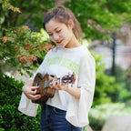 Acoustic Four-String Ukulele player in a white shirt strumming the striped brown version from an angle.