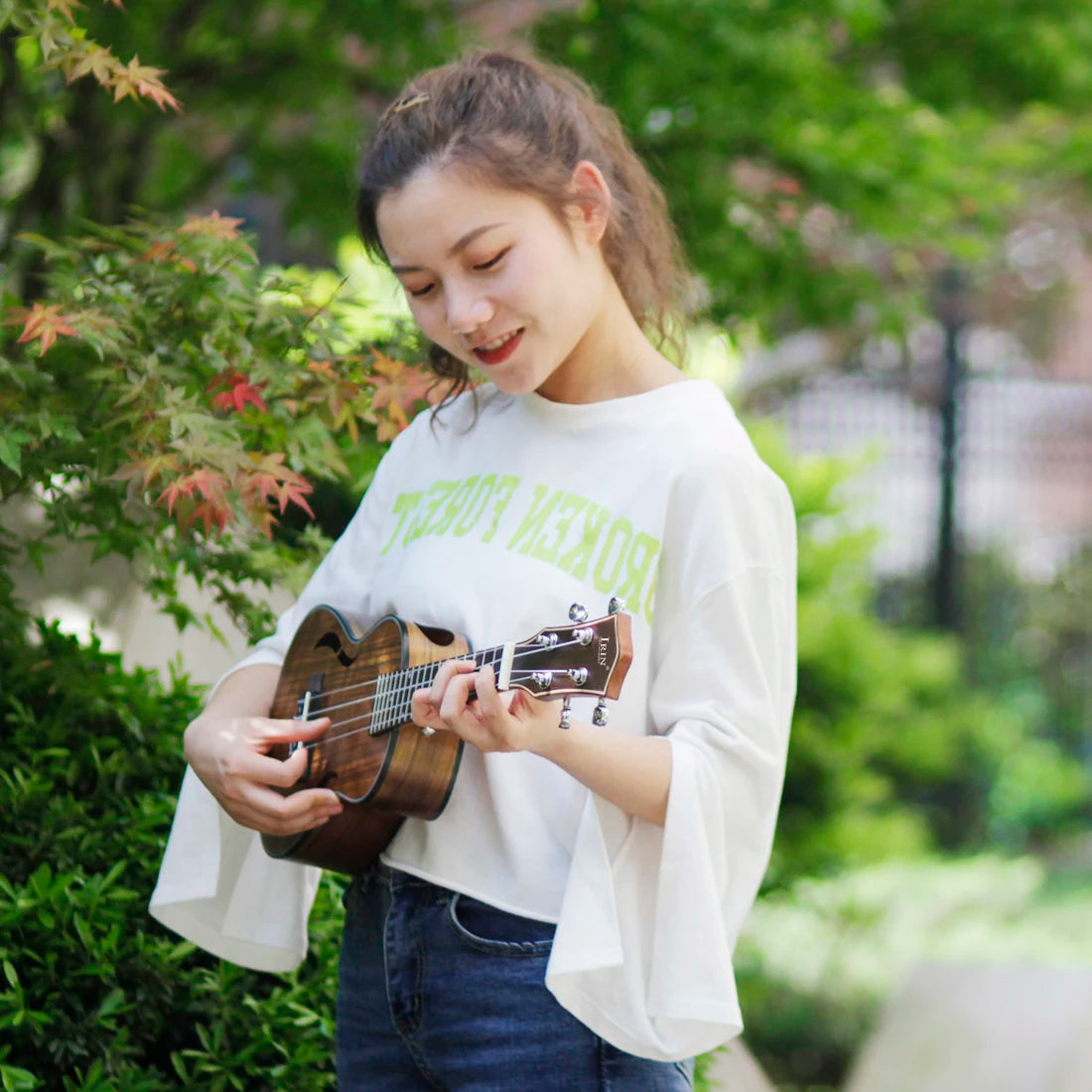 Acoustic Four-String Ukulele player in a white shirt strumming the striped brown version from an angle.