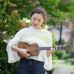 Acoustic Four-String Ukulele front view of a player holding the striped brown version outdoors.