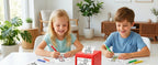 AI Voice Sticker Box on a table while two children color printed line drawings together