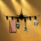 Airplane Key Holder on an amber wall under warm lighting, with keys and a tan pouch hanging from its hooks.